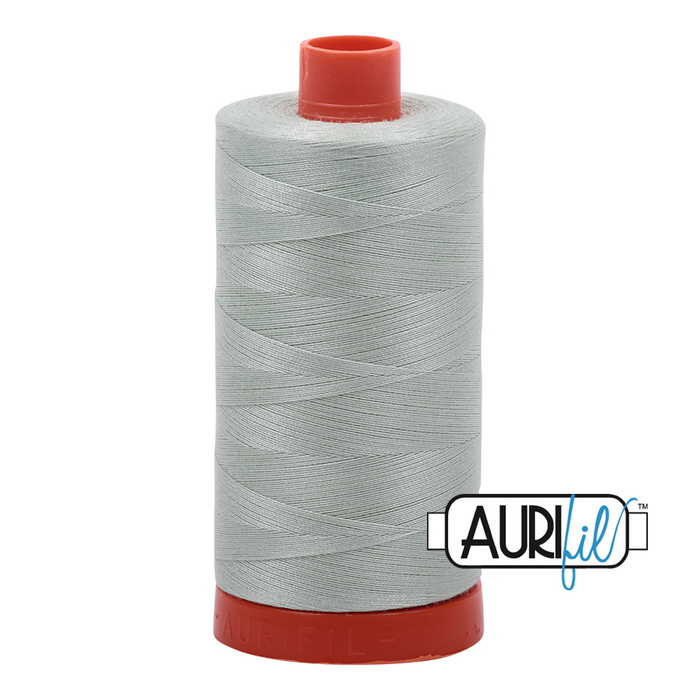 A spool of Aurifil 50wt platinum thread with a grey hue and red cap.