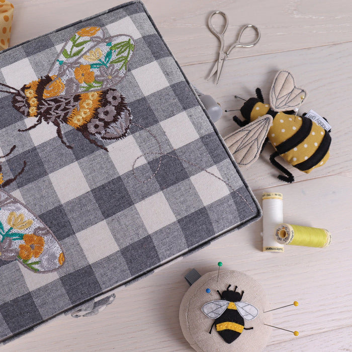 Embroidered fabric with bee design on a checkered background, surrounded by sewing tools and Pin cushion with bee design