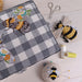Embroidered fabric with bee design on a checkered background, surrounded by sewing tools and Pin cushion with bee design