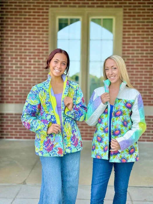 Two women wearing colorful jackets standing in front of a brick building. Bella Quilt Coat pattern 