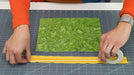 Person measuring green fabric with a ruler on a cutting mat