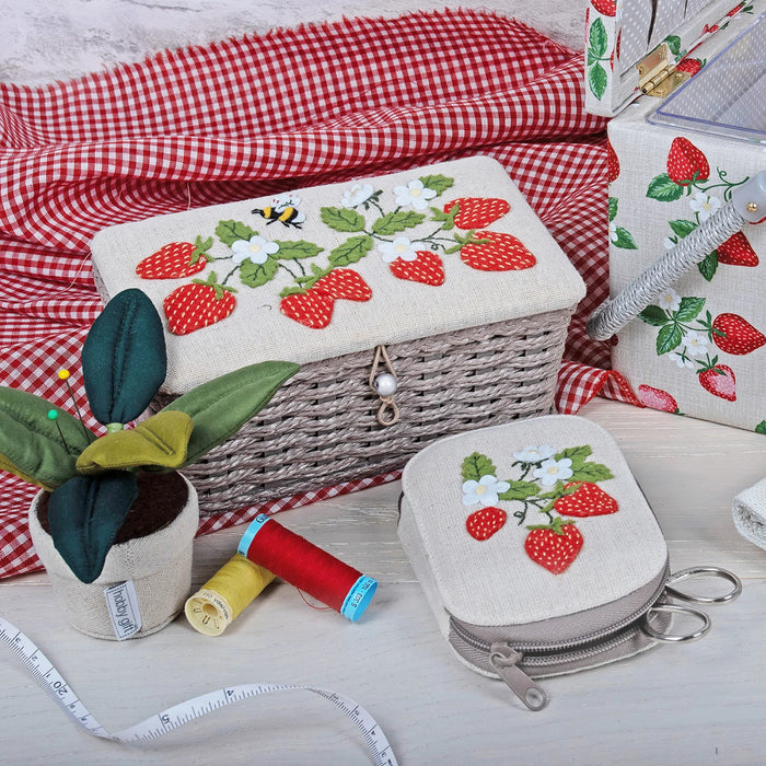 Embroidered strawberry designs on fabric pieces with a red and white checkered cloth in the background.