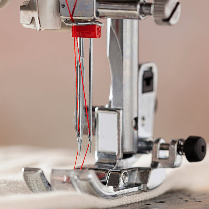 Close-up of a Schmetz double hemstitch sewing machine needle and thread on a beige background