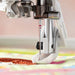 Close-up of a Schmetz sewing machine needle piercing fabric with a colorful background