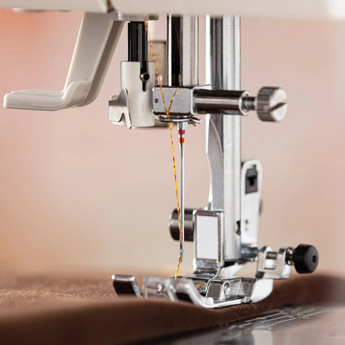 Close-up of a Schmetz metallic sewing machine needle and thread on a wooden surface with a blurred background.