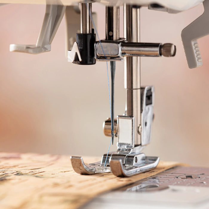 Close-up of a sewing machine needle and foot on a wooden surface with a blurred background.