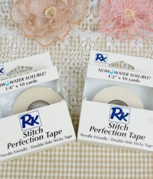 Two packages of RNK Stitch Perfection Tape on a textured surface with floral decorations.